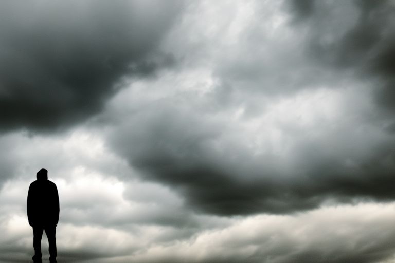 A closeup image of a person looking determinedly ahead while standing against a backdrop of stormy clouds