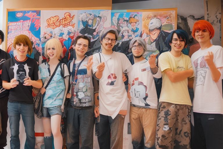 A group of friends posing together in front of an anime poster at an anime convention