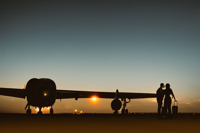A photo depicting two silhouettes standing next to an airplane on a runway at night with lights shining brightly around them