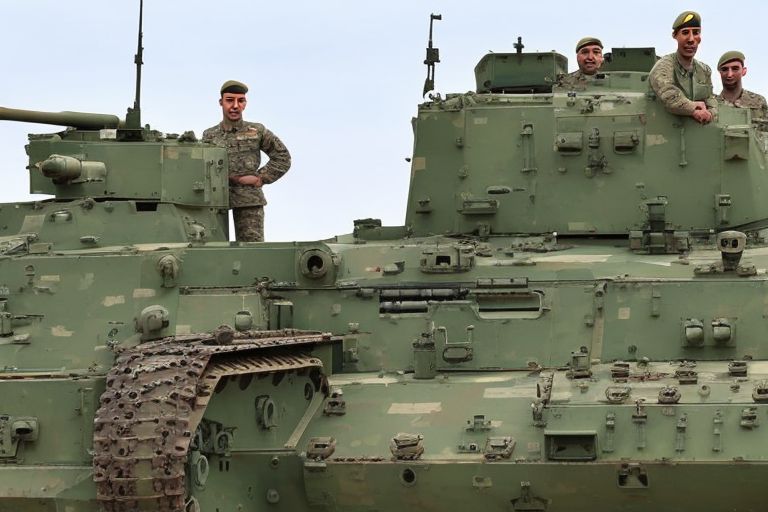 A photo of soldiers standing beside an olive green Sabrah light tank with its turret pointed towards camera